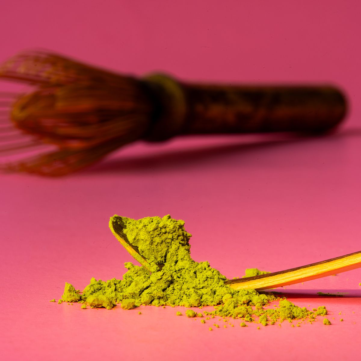 Matcha-Pulver mit Bambuslöffel und Matcha-Besen auf rosa Hintergrund