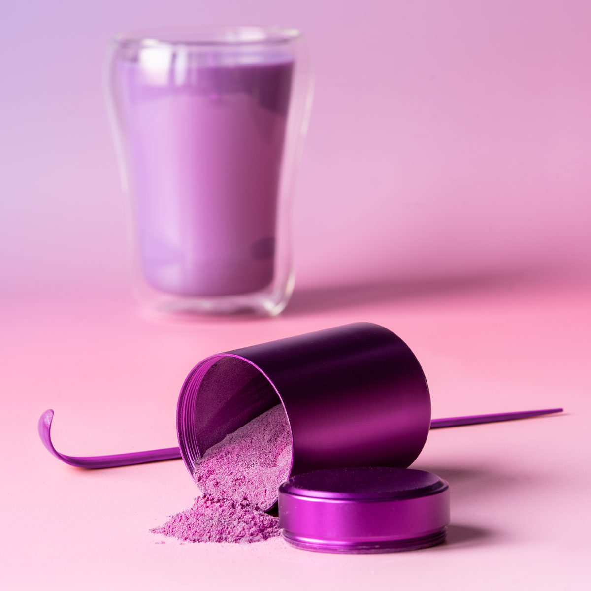 Ube-Pulver aus violetter Dose verschüttet, dahinter ein Glas Ube Latte