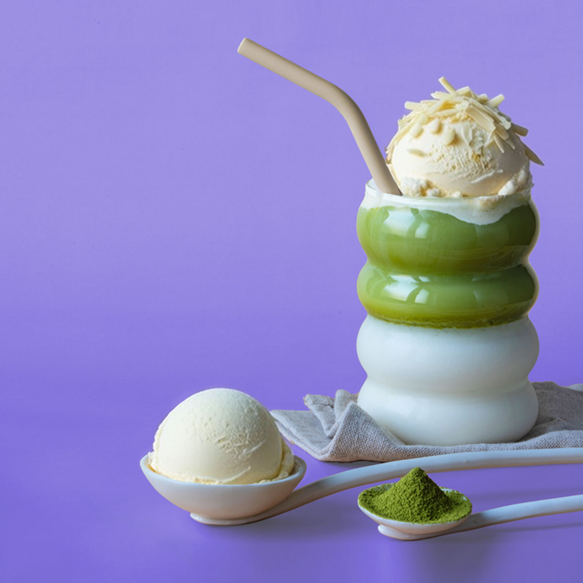 Vanille-Matcha-Getränk mit Eiskugel und Matcha-Pulver vor violettem Hintergrund